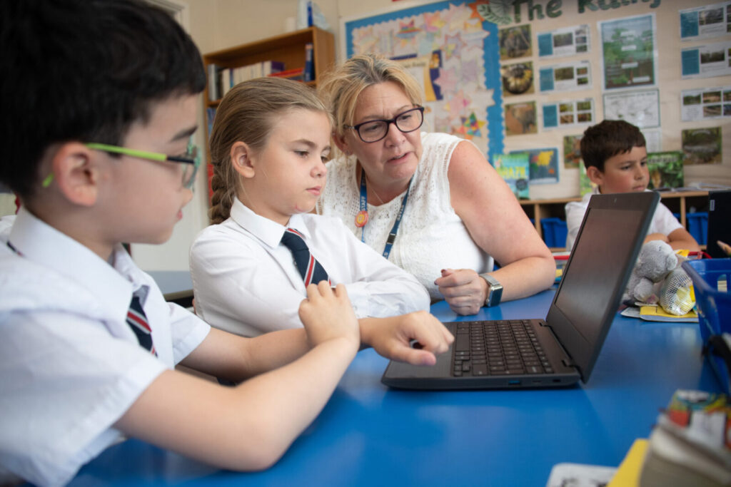 a picture of a teacher helping students on the laptop